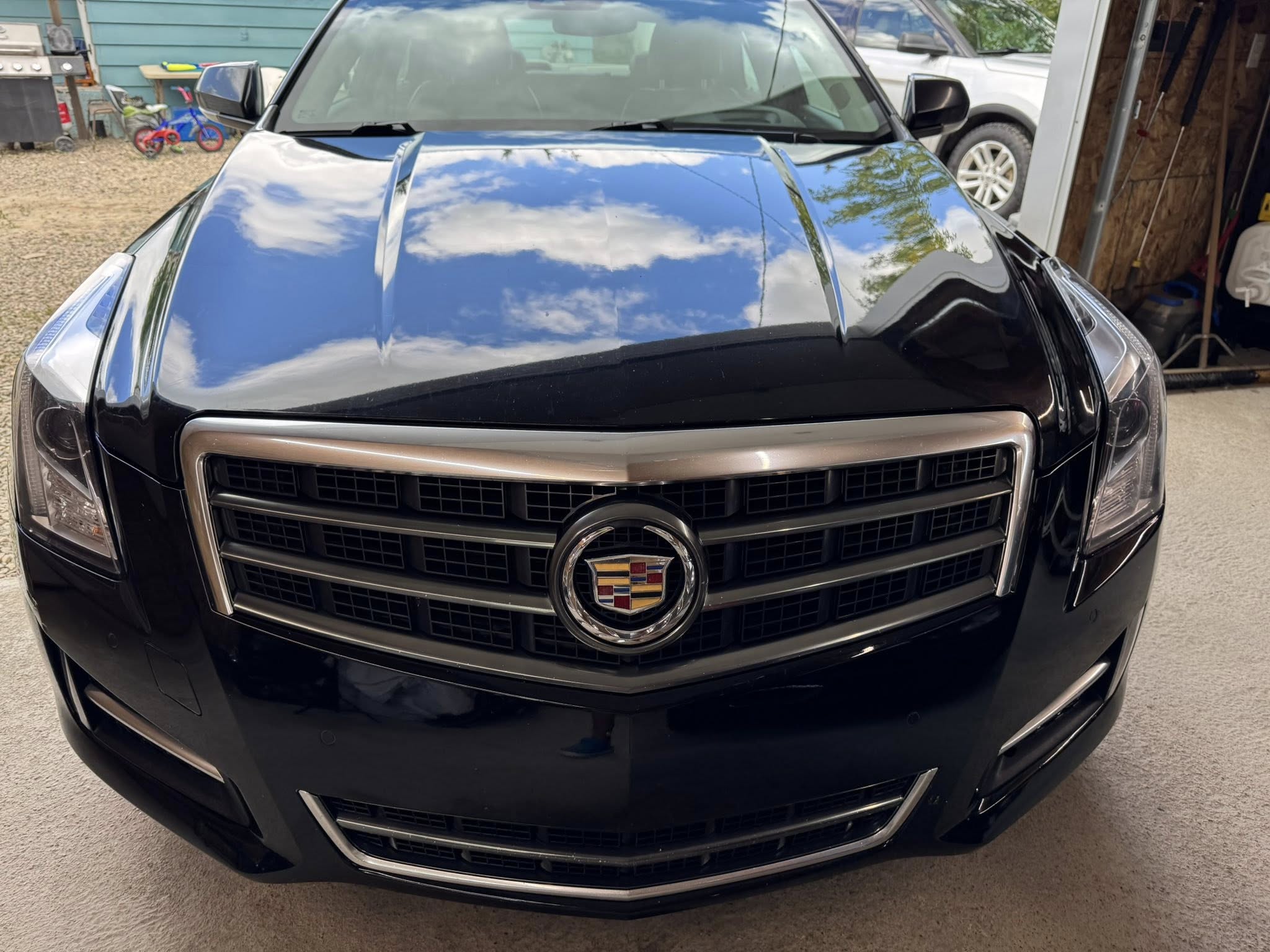 Freshly detailed black Cadillac with a polished hood reflecting the sky.